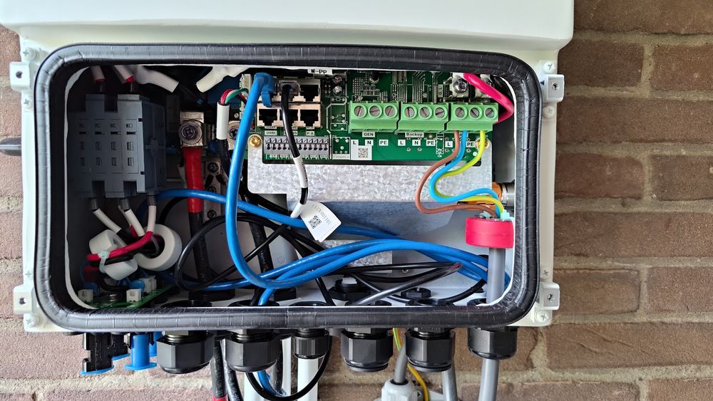 Een geopende aansluitkast aan een bakstenen gevel met ingevoerde kabels