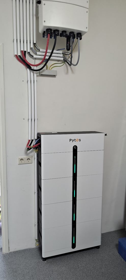 Een accu op de vloer met de omvormer erboven, de kabels netjes in witte goten
