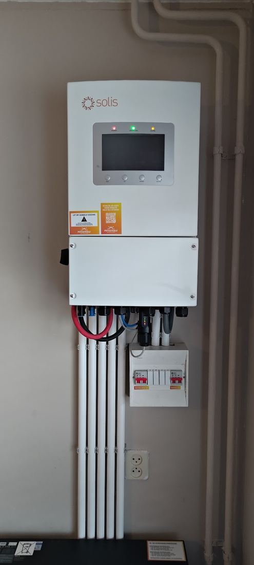 Een omvormer met display aan de muur, met kabelbuizen recht omlaag