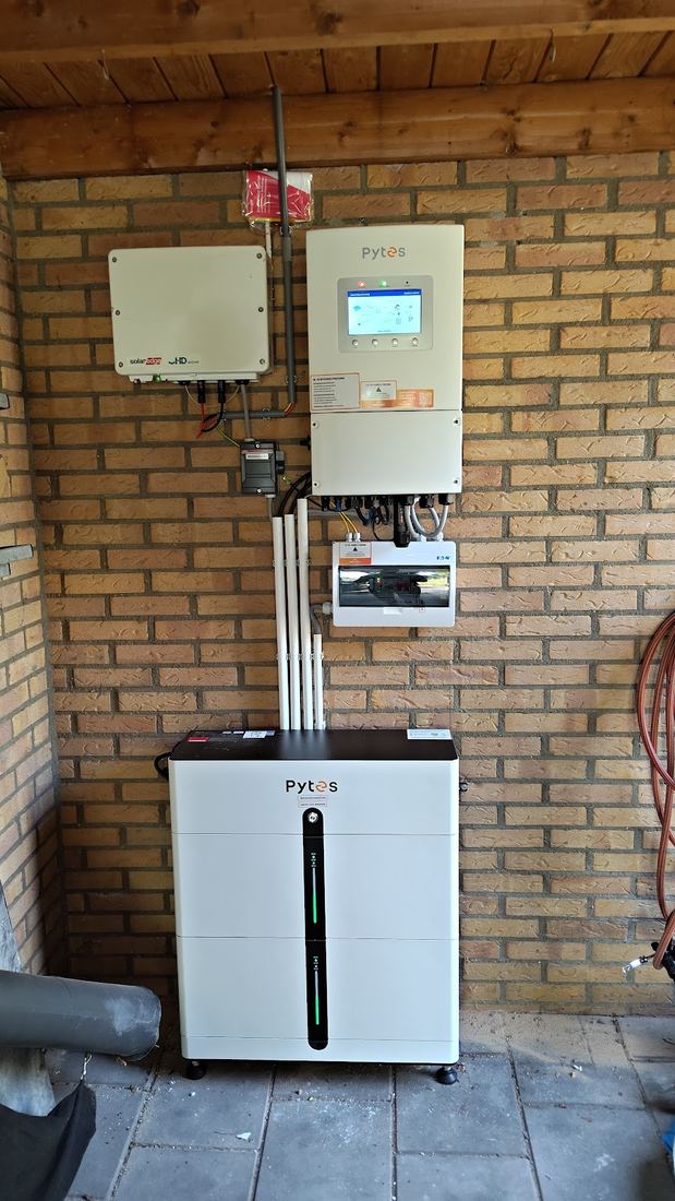 Een accu met omvormer en verdeelkast tegen een bakstenen muur in een garage