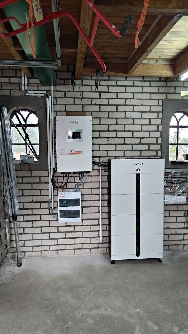 Een garagewand met omvormer, groepenkast en een witte accu